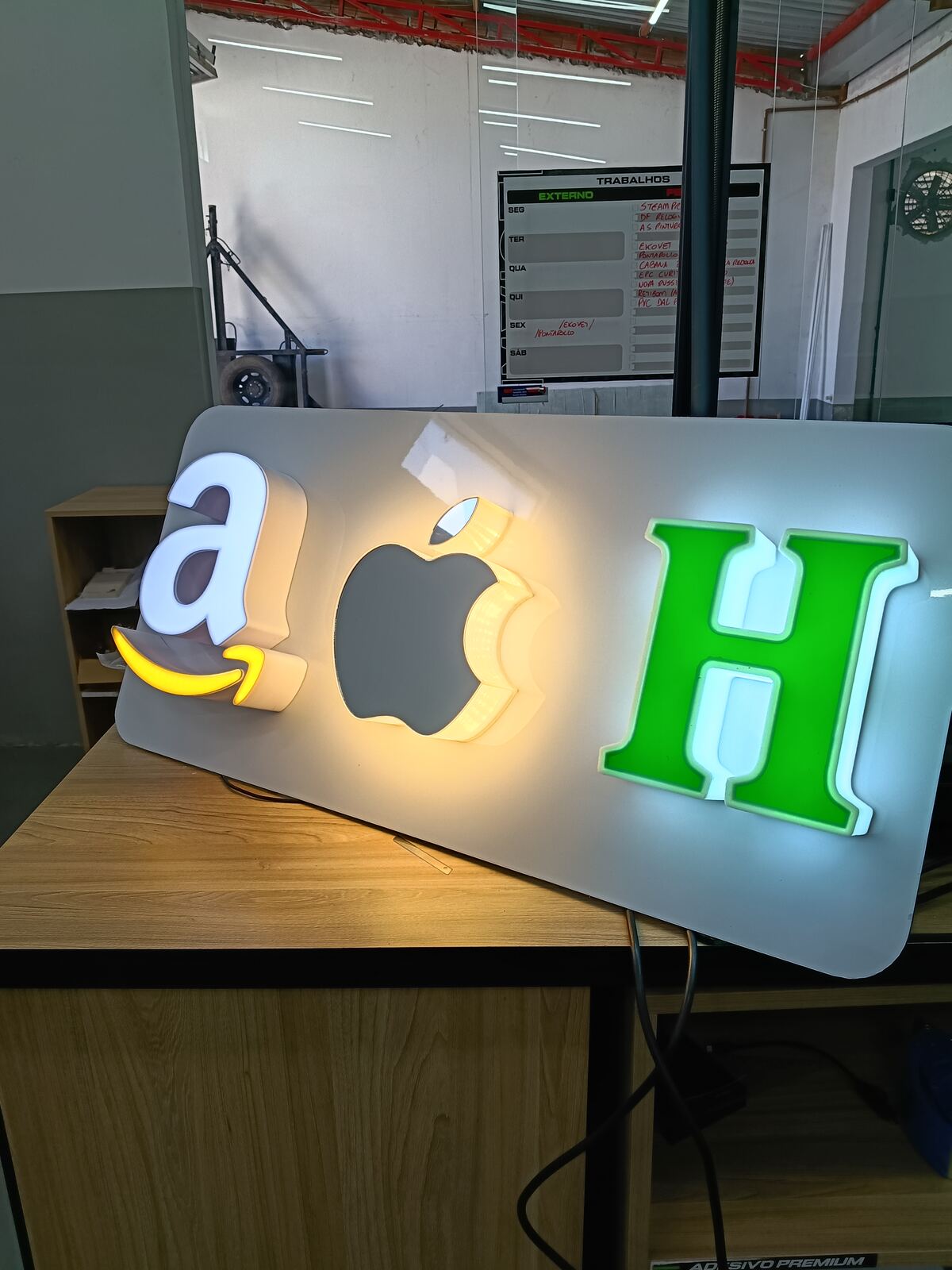 Letras caixa iluminadas com os logos Amazon, Apple e a letra H